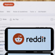 A phone bearing Reddit's logo in front of a screen showing the NBA reddit page.